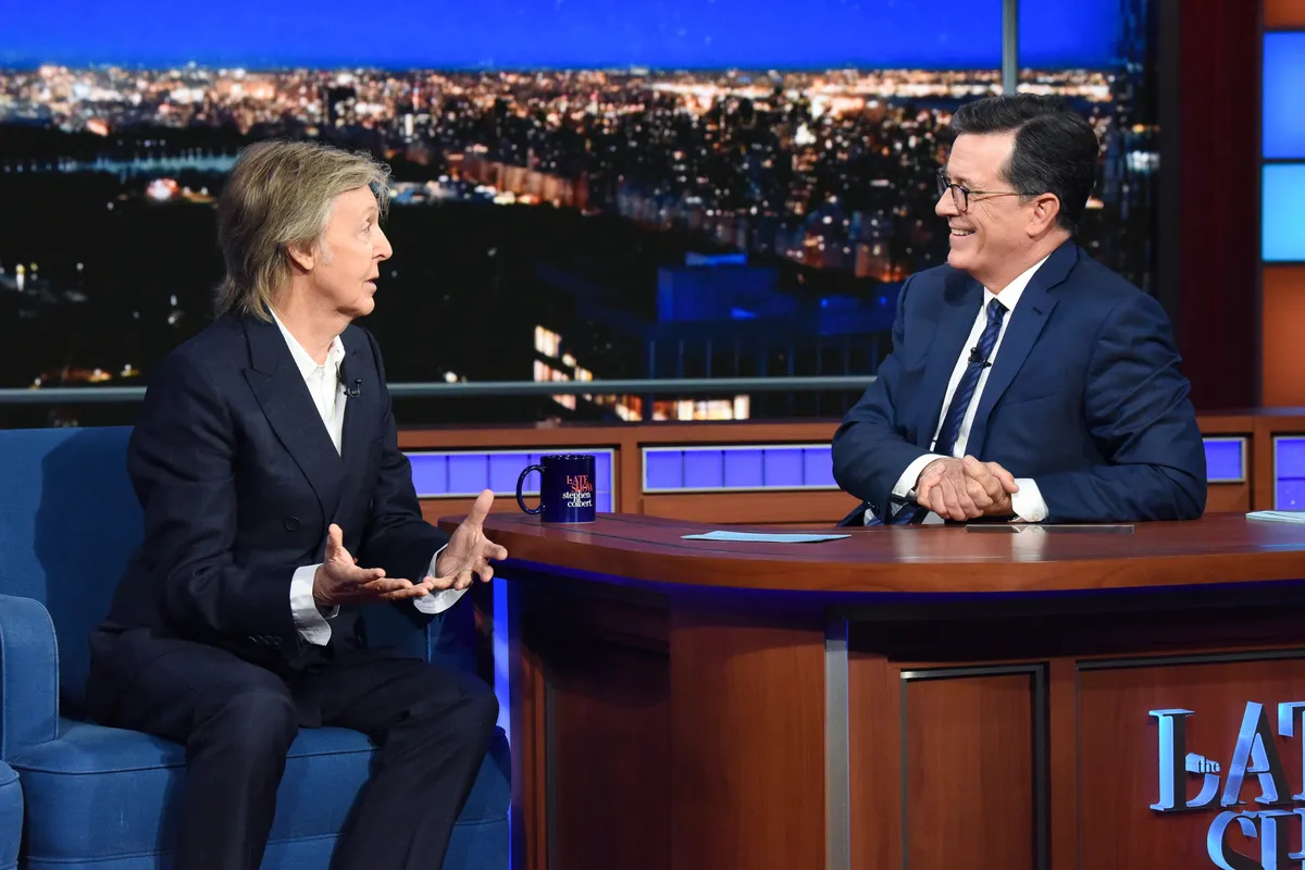 Stephen Colbert smiling on The Late Show stage with guests.