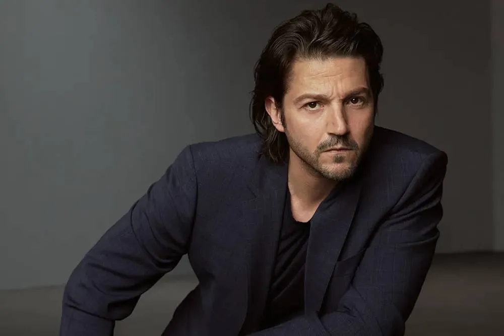 Diego Luna smiling, against a background hinting at the whimsical, magical world of Tangled with glowing lanterns.