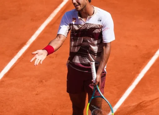 A tennis player on a red clay court looking frustrated during a match.
