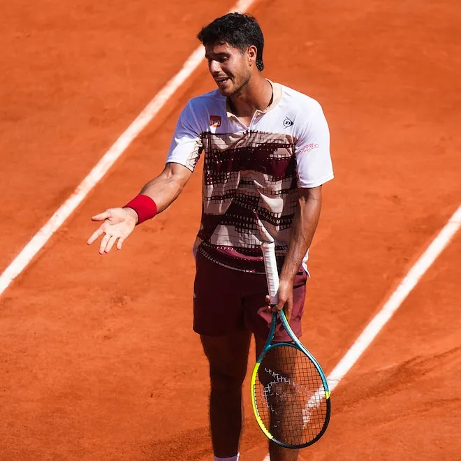 A tennis player on a red clay court looking frustrated during a match.