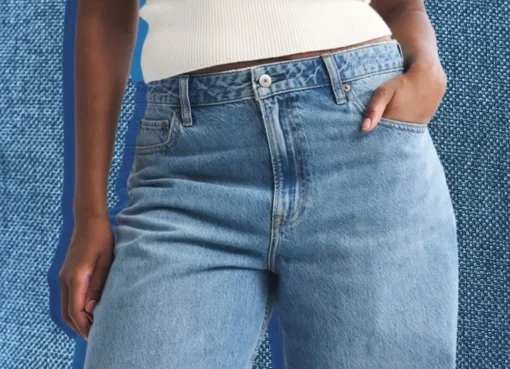 A smiling woman wearing well-fitting midsize jeans, showing no waist gap.
