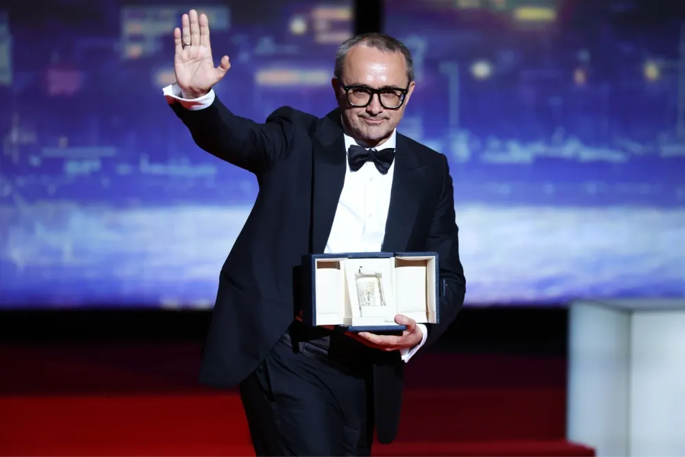 Andrey Zvyagintsev on stage at the Cannes Film Festival, holding an award and speaking into a microphone.