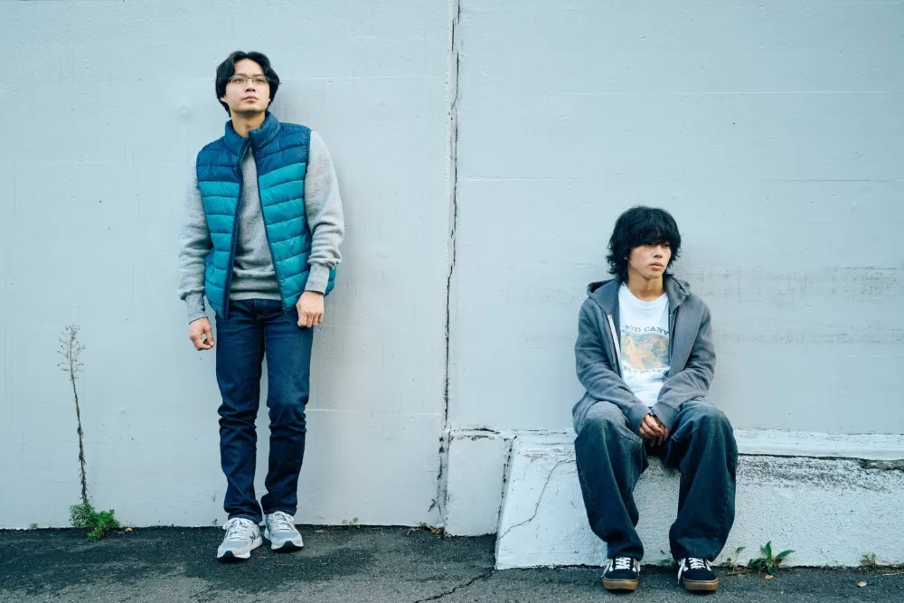 A dark, intense film still from a Japanese drama showing a somber, emotional scene.