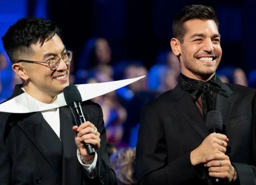 Bowen Yang and Matt Rogers standing on a bright, colorful stage during the Las Culturistas Culture Awards.