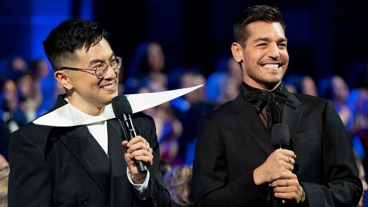 Bowen Yang and Matt Rogers standing on a bright, colorful stage during the Las Culturistas Culture Awards.