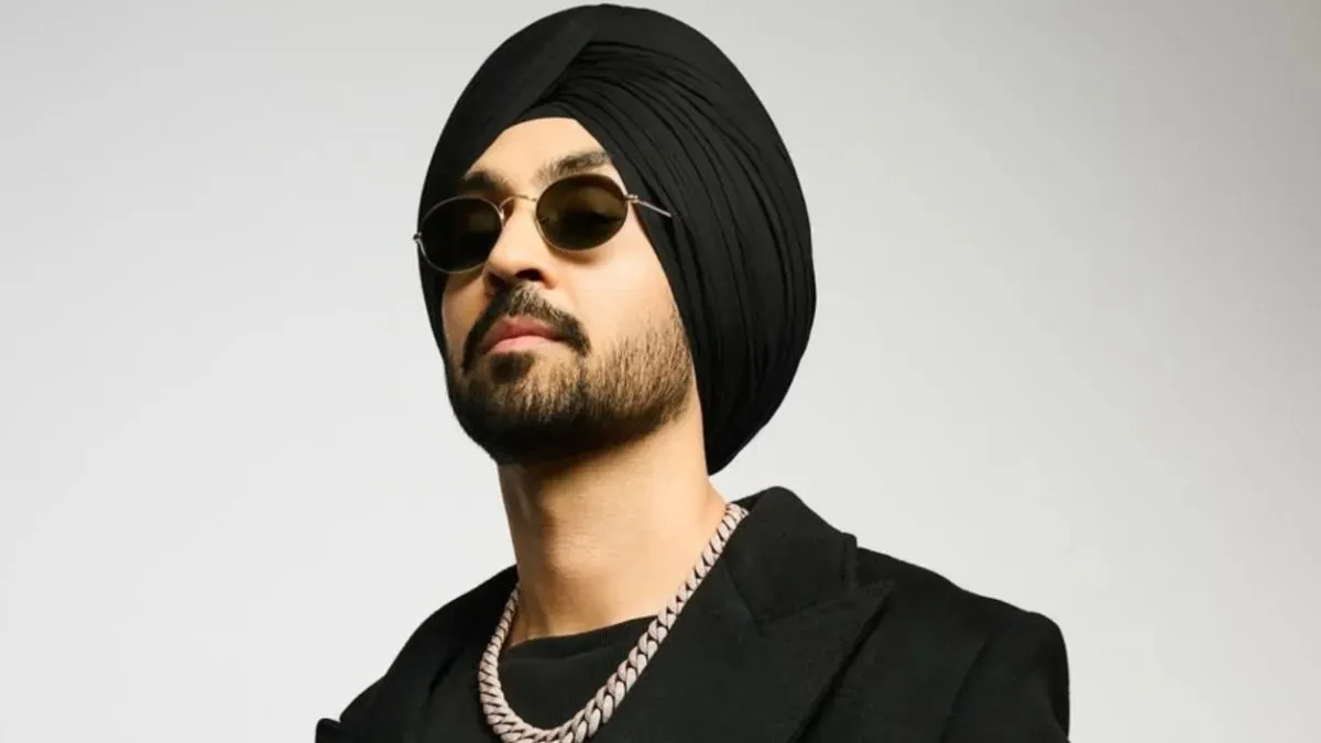 Diljit Dosanjh smiling and waving to a crowd during a performance.