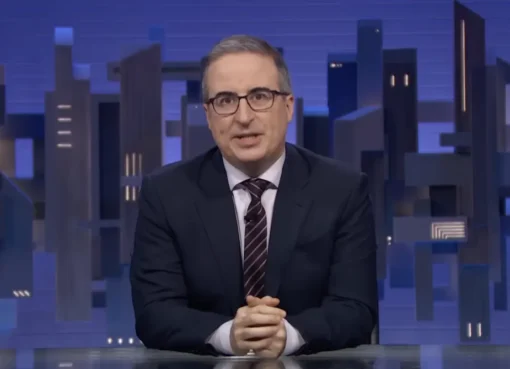 John Oliver on his TV show set, looking animated.