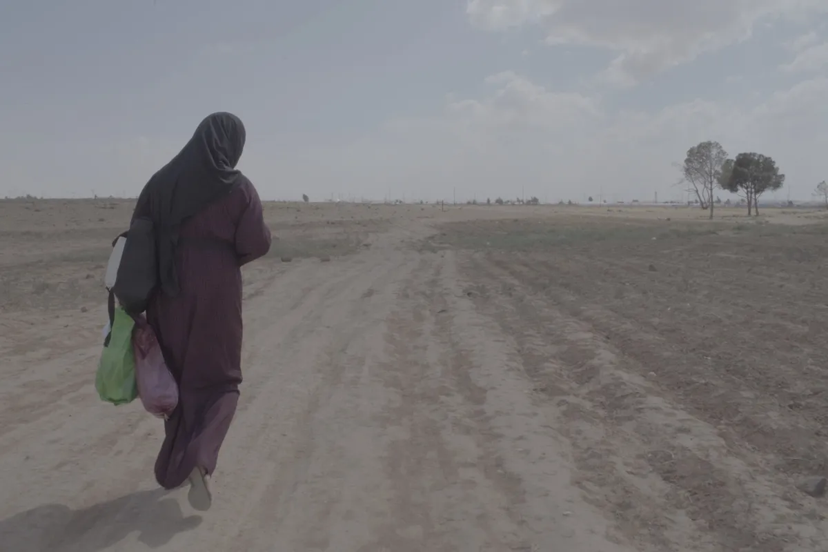A film camera on a tripod capturing a scene in an arid, sandy setting.