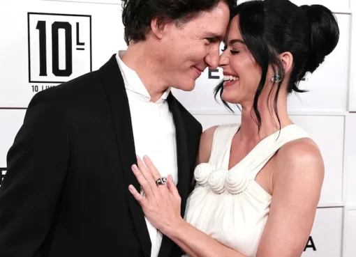 Katy Perry smiling happily with Justin Trudeau, bathed in warm light.