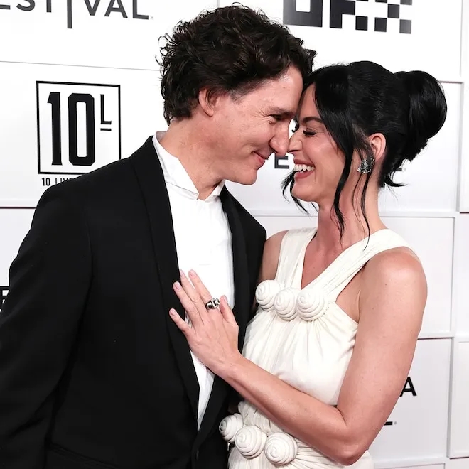 Katy Perry smiling happily with Justin Trudeau, bathed in warm light.