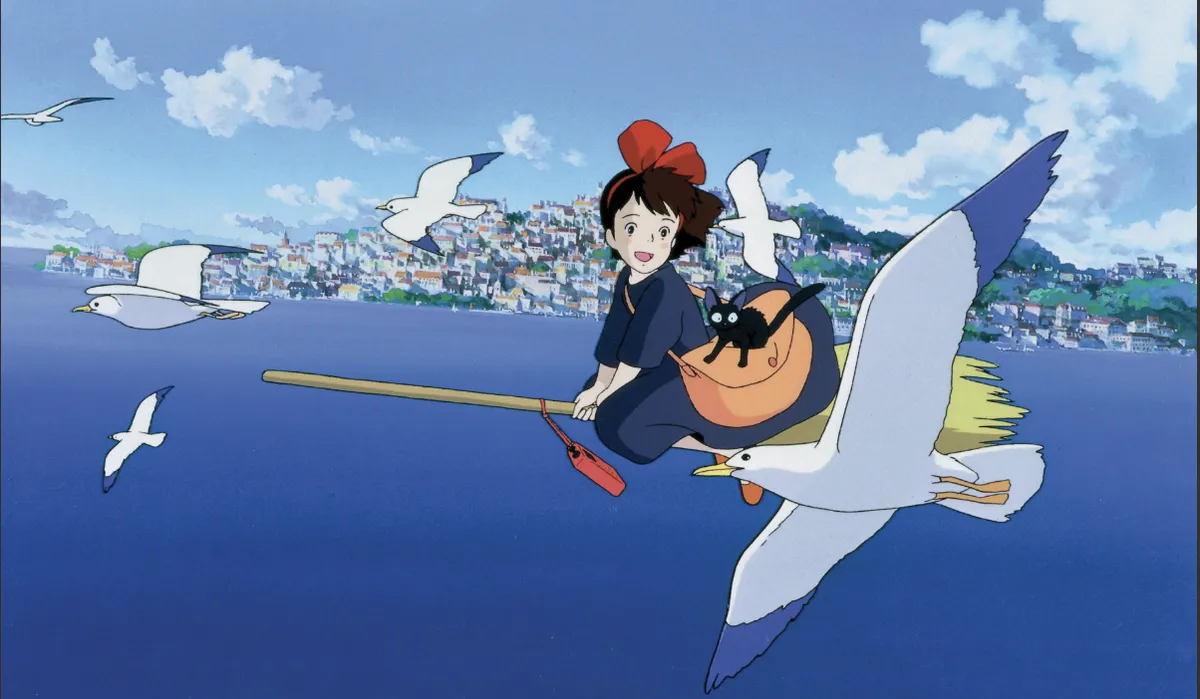 Illustration of Kiki flying on her broomstick with her black cat Jiji against a bright, European-inspired sky.