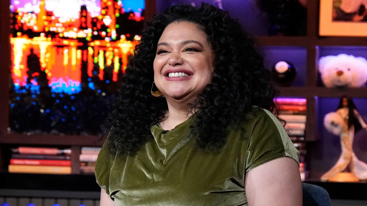 Michelle Buteau laughing and smiling during a talk show appearance.