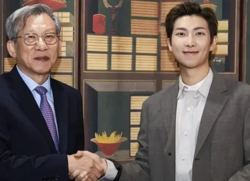 RM from BTS smiling while looking thoughtful, possibly in a museum setting.