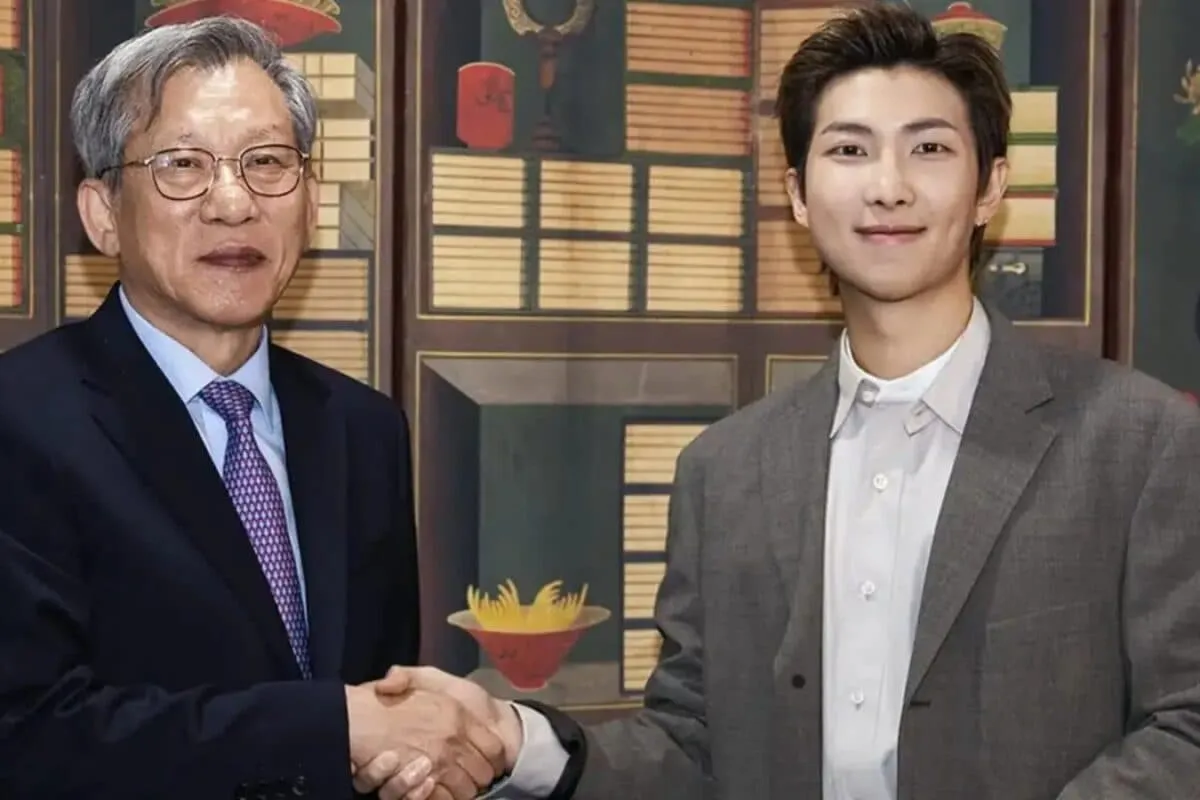 RM from BTS smiling while looking thoughtful, possibly in a museum setting.