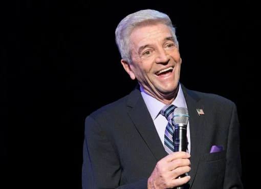 A black and white portrait of comedian Tom Dreesen smiling