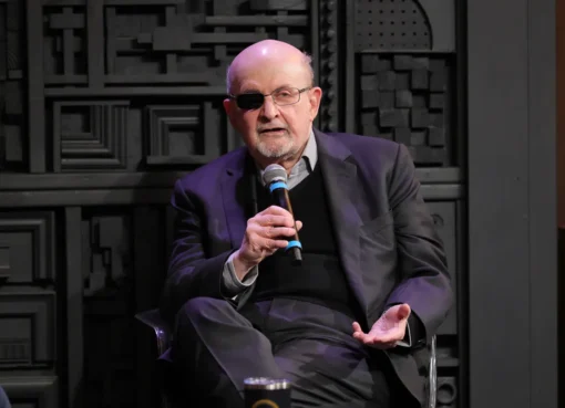 Salman Rushdie smiling and talking at a podium during a literary festival