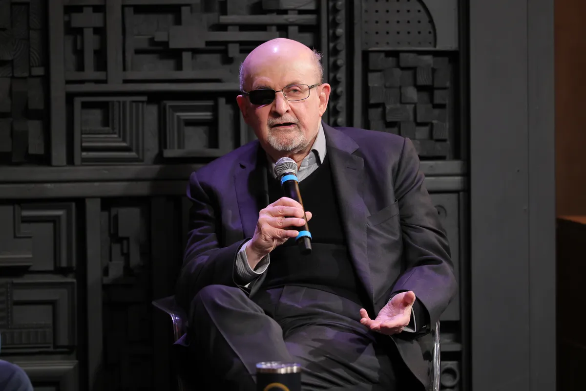 Salman Rushdie smiling and talking at a podium during a literary festival