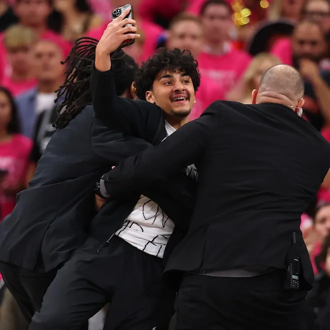 Fans running onto a basketball court during an NBA game.