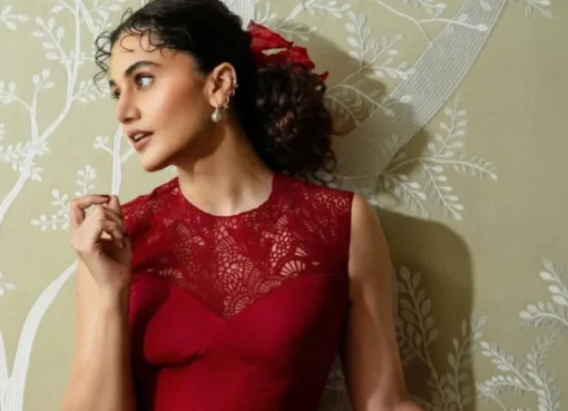 Taapsee Pannu smiling, wearing a stylish outfit, against a blurred background.
