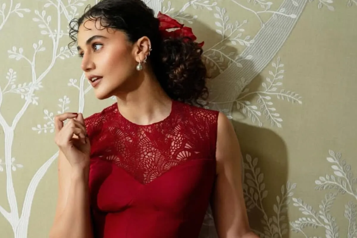 Taapsee Pannu smiling, wearing a stylish outfit, against a blurred background.