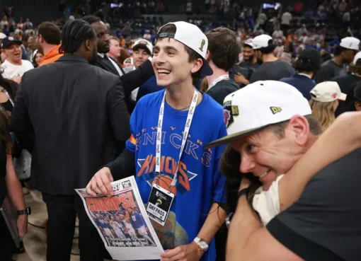 Timothée Chalamet smiling and looking excited courtside at a basketball game.