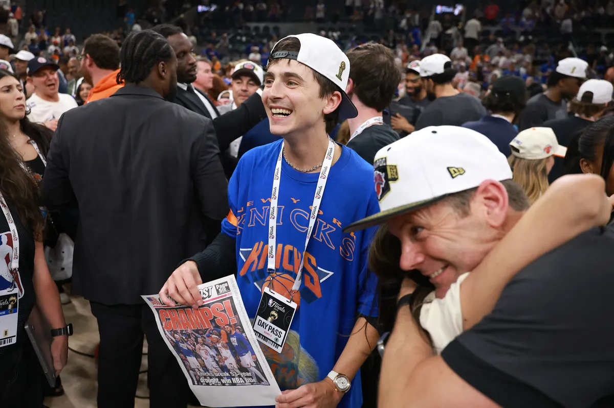 Timothée Chalamet smiling and looking excited courtside at a basketball game.