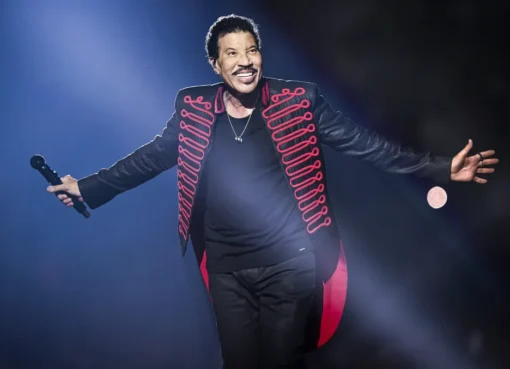 Lionel Richie singing on stage under colorful lights, holding a microphone.