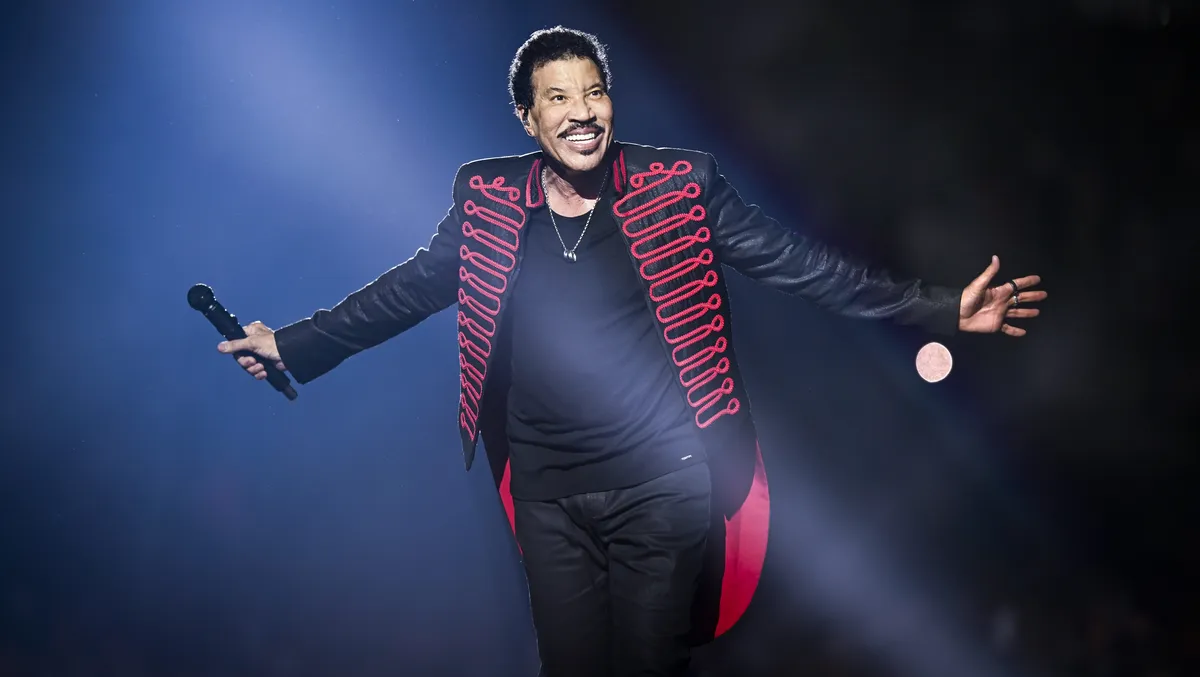 Lionel Richie singing on stage under colorful lights, holding a microphone.