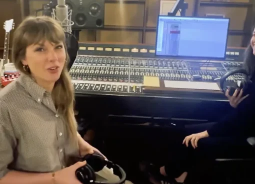 Taylor Swift smiling, possibly in a recording studio, looking happy and creative.