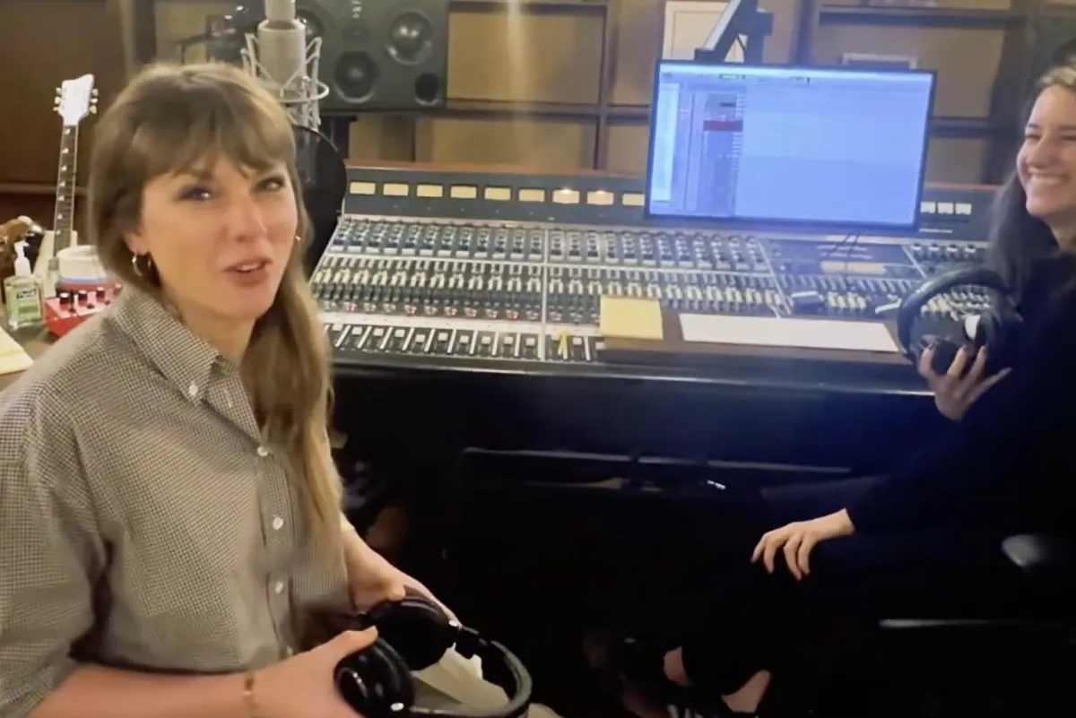 Taylor Swift smiling, possibly in a recording studio, looking happy and creative.