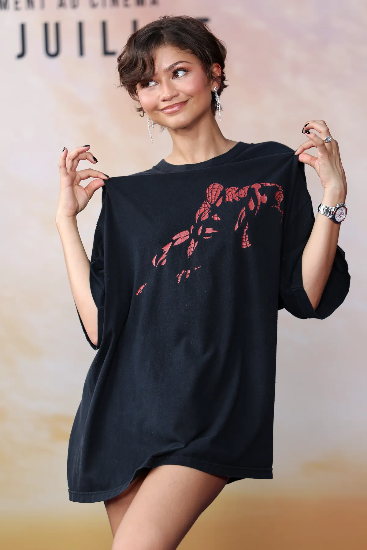 Zendaya smiling in an oversized black Spider-Man t-shirt at a fan event.