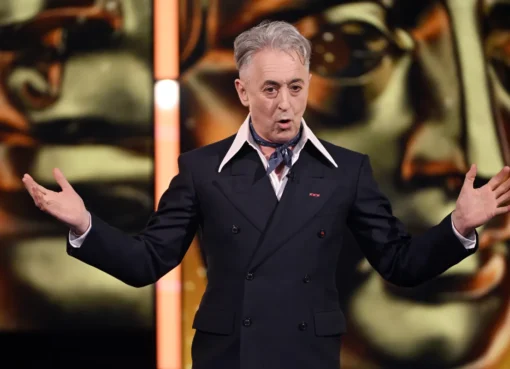 Alan Cumming looking thoughtful and determined, with a backdrop of a film set or movie reels, suggesting a fight for independent cinema.