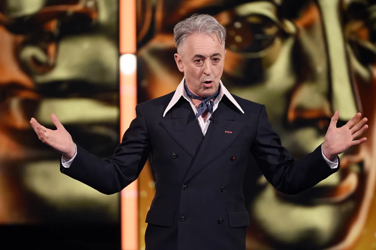 Alan Cumming looking thoughtful and determined, with a backdrop of a film set or movie reels, suggesting a fight for independent cinema.