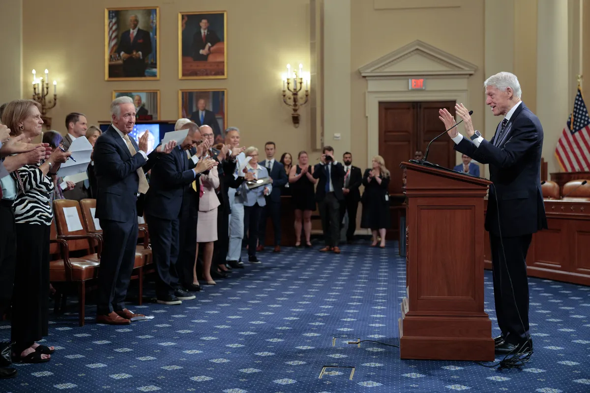 Bill Clinton speaking at an event, looking serious.