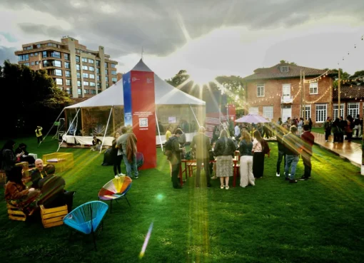 A group of diverse young filmmakers networking at the Bogotá Audiovisual Market, with film equipment and colorful banners in the background.