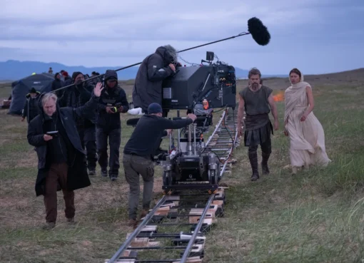 Christopher Nolan on a film set, looking at a large camera.