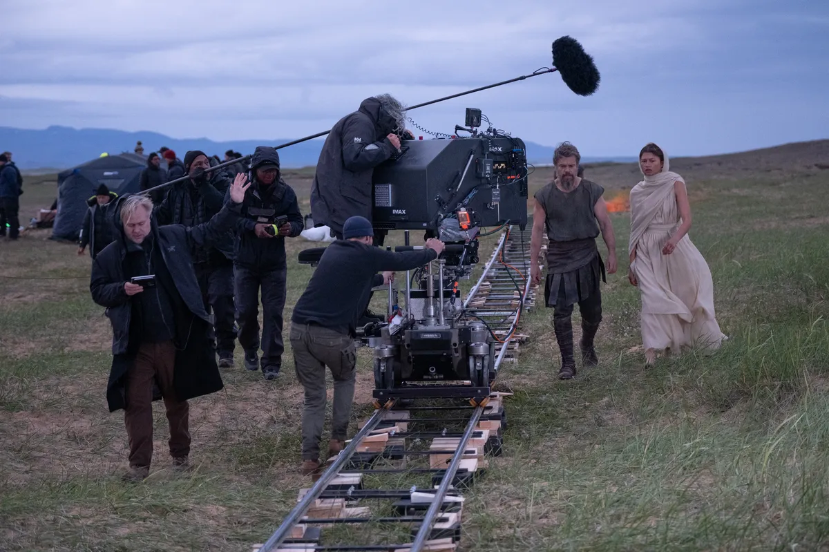 Christopher Nolan on a film set, looking at a large camera.