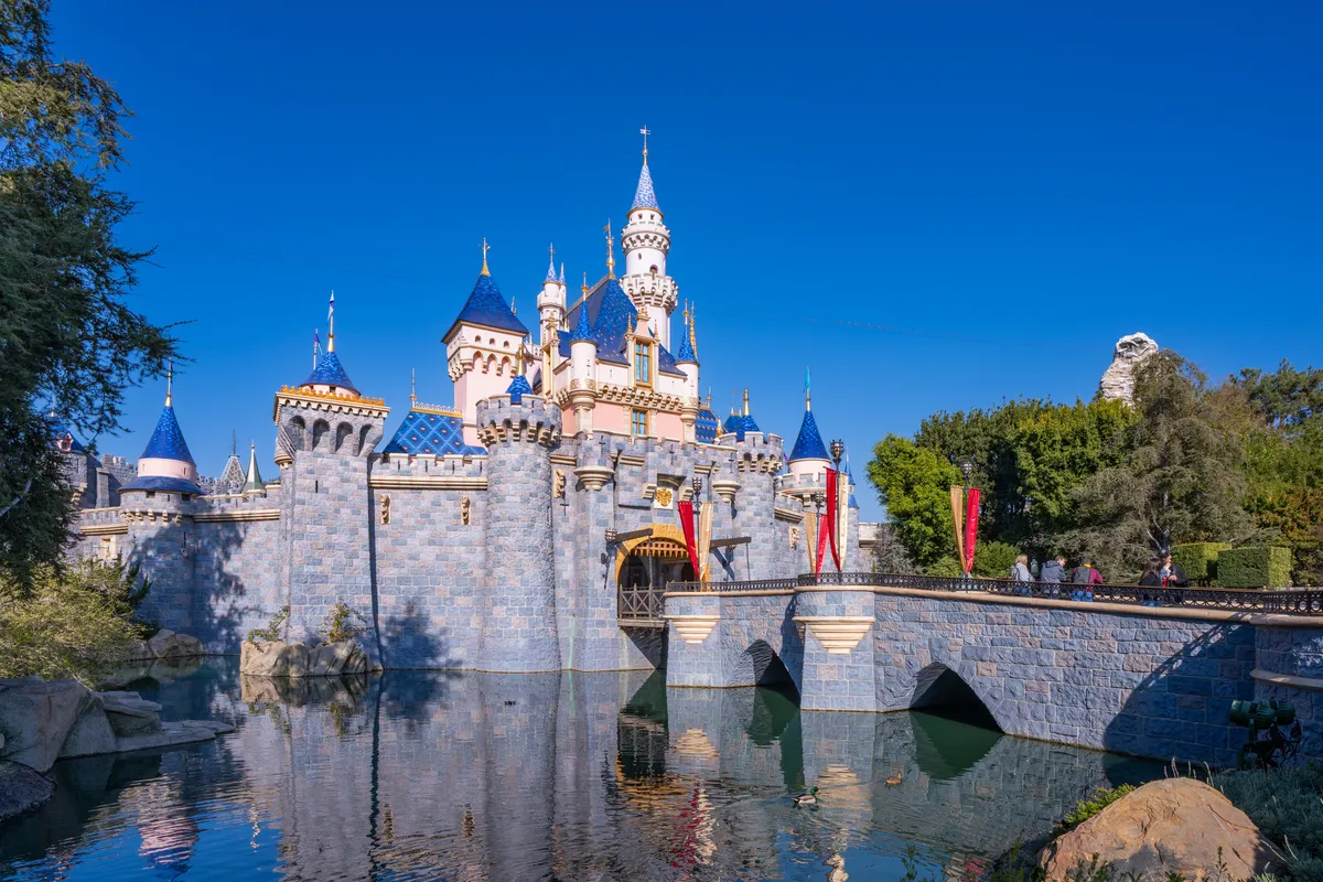 The Disneyland castle lit up with colorful lights at night during the summer