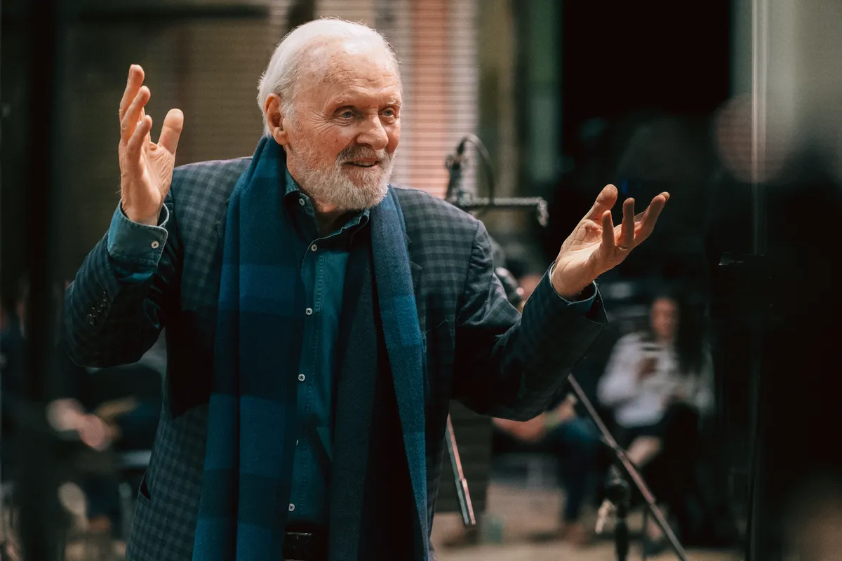 Anthony Hopkins looking thoughtful, possibly in a recording studio or with sheet music, with a serious but reflective expression.