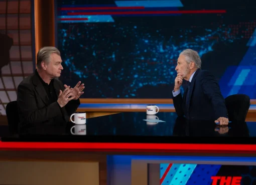 Christopher Nolan and Jon Stewart sharing a laugh on The Daily Show set.