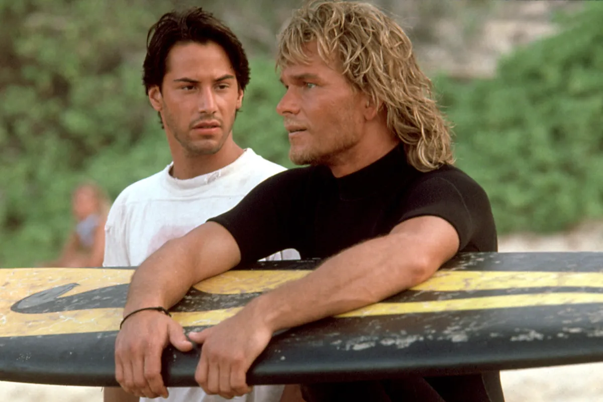 Keanu Reeves and Patrick Swayze riding a wave with surfboards in the movie Point Break.