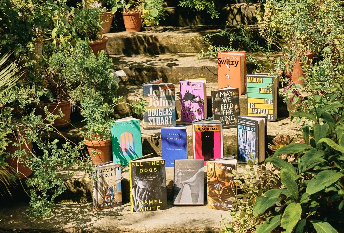 A stack of thick novels with colorful artistic covers sitting on a clean white shelf.