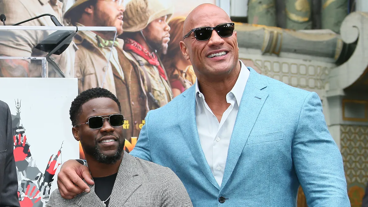 Dwayne Johnson and Kevin Hart smiling together, looking like they're about to tell a joke.