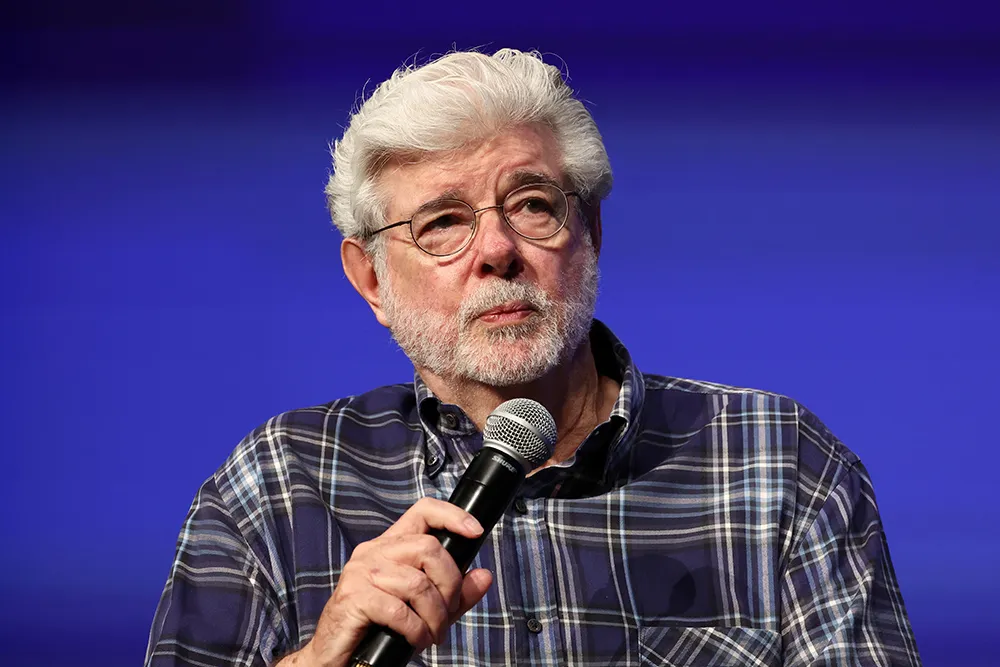 George Lucas smiling thoughtfully, perhaps gesturing during an interview.