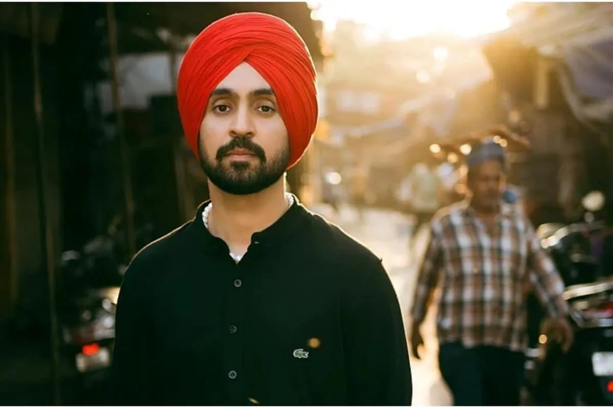 Diljit Dosanjh looking thoughtful and charismatic, possibly on a stage or at an event, with a slight smile.