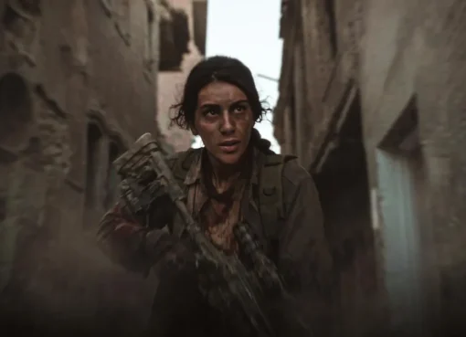 A still from a drama showing a determined female sniper, possibly in a desert or urban conflict zone, with a rifle.