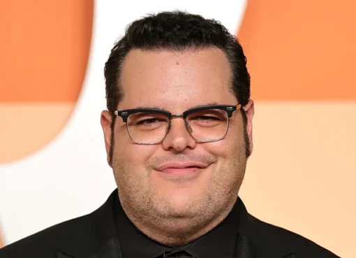 Josh Gad smiling, with blurred images of Margot Robbie and Bradley Cooper in the background.