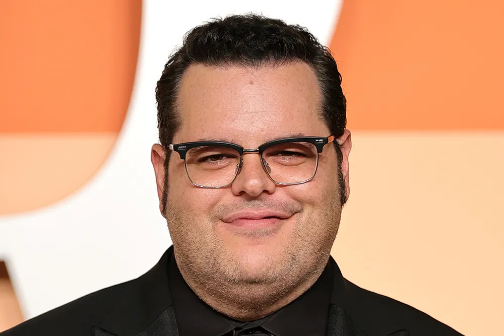 Josh Gad smiling, with blurred images of Margot Robbie and Bradley Cooper in the background.