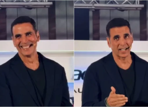 Akshay Kumar laughing heartily at a press conference, looking amused and relaxed.