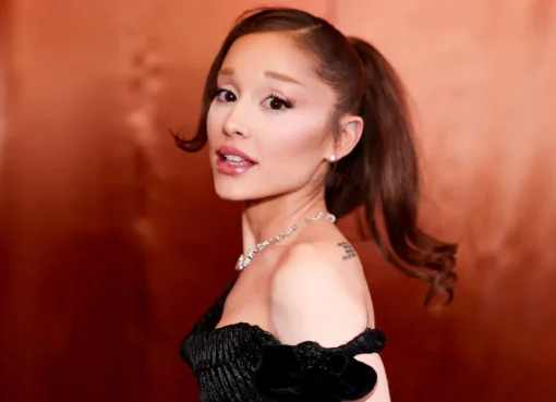 Ariana Grande performing on stage, singing into a microphone with bright lights in the background.